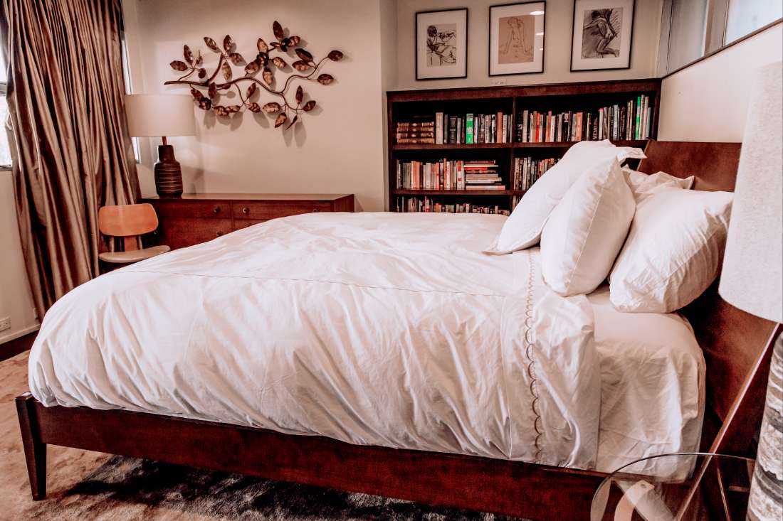 A bed with white sheets and pillows in front of a bookshelf.