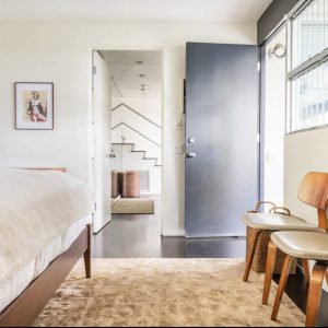 A bedroom with a bed, chair and stairs leading to the second floor.