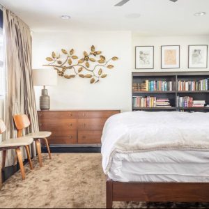 A bedroom with a bed, chair and bookshelf.
